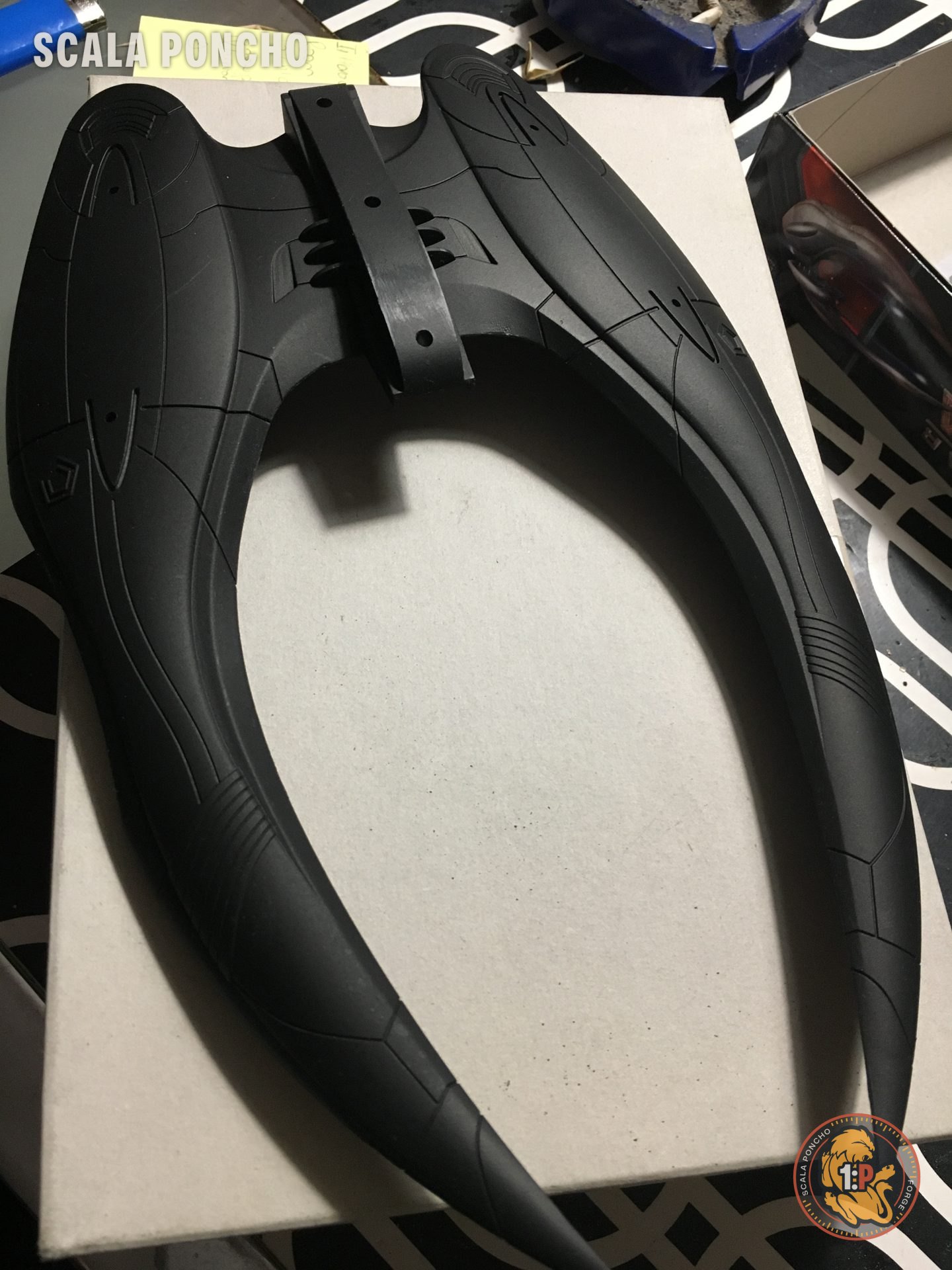 Scafo a mezzaluna del Cylon Raider in plastica nera appoggiato su un cartone