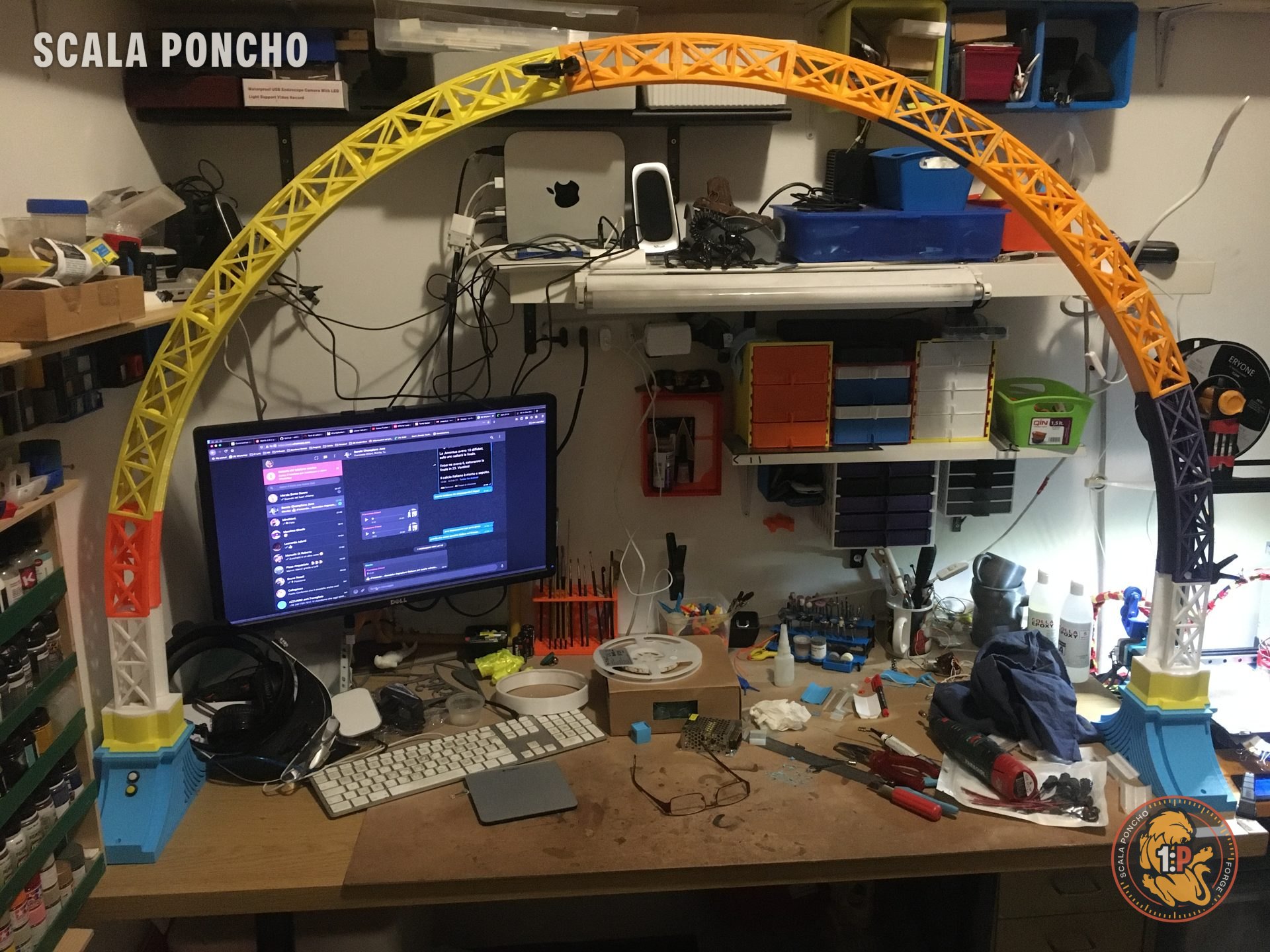 Arco reticolare stampato in 3D appena montato sopra la scrivania, segmenti in colori diversi, appoggiato su due supporti blu