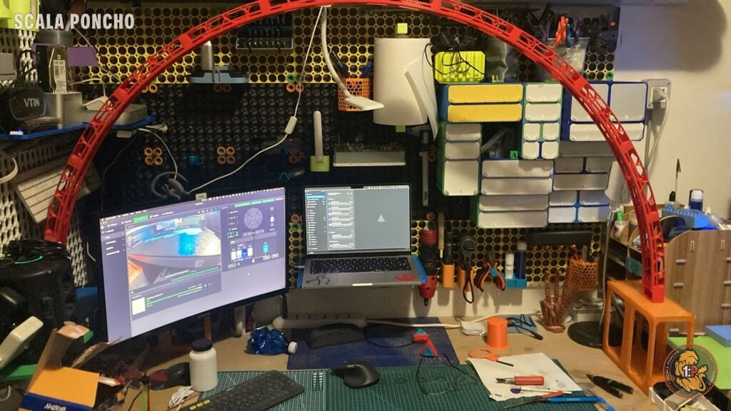 Nuovo arco reticolare rosso stampato in 3D sopra la postazione con monitor curvo, portatile e pannelli forati con cassettiere stampate