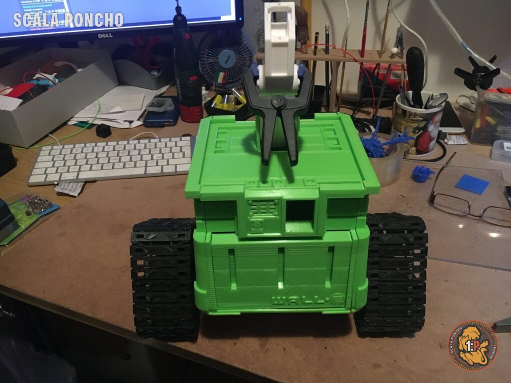 Corpo di WALL-E stampato in 3D in filamento verde sopra i cingoli neri, sul banco di lavoro